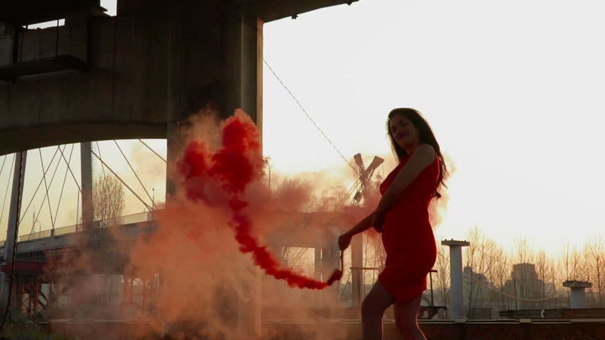 Gorgeous woman with red smoke flare dancing under abandoned bridge