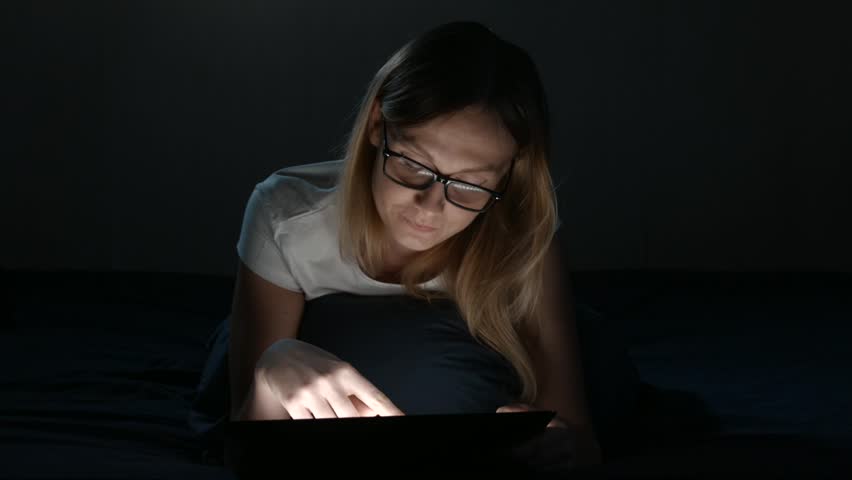 Girl with glases is lying in a bedroom and using digital tablet. Isolated Black. Front view. insomnia
