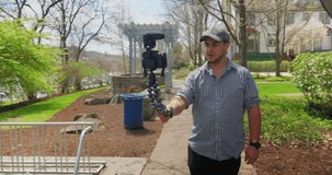 A millennial vlogger influencer wearing a baseball cap backwards holds his DSLR camera 
