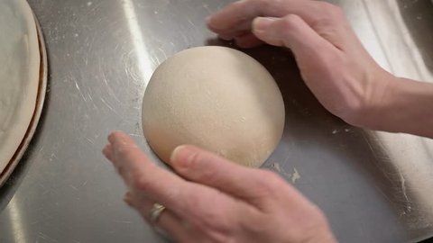 The hands of the chef knead the dough on the desktop in the restaurant kitchen