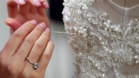Close-up fashion designer for brides in his Studio pins needles lace wedding dress. Seamstress creates an exclusive wedding dress. Secure with pins and needles outline. Small private business.