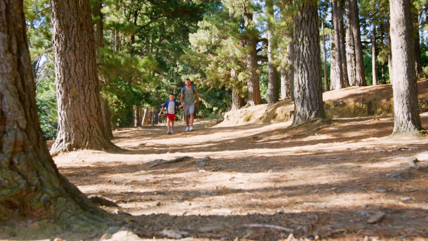 Father And Son On Hiking Adventure Running Through Forest