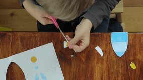 Boy cutting colored paper with scissors at the table, top-view video