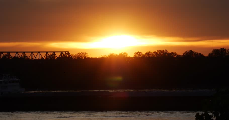 Fiery orange vivid sunset on the Mississippi River Memphis Tennessee with a cargo boat cruising past in the foreground and a silhouetted bridge