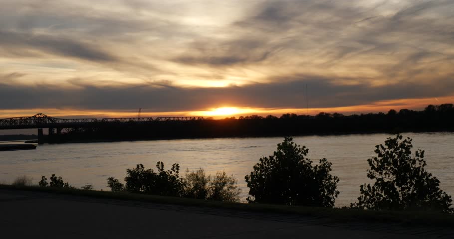 Fiery orange sunset over the Mississippi River on a cloudy evening reflected off the calm water below Memphis Tennessee