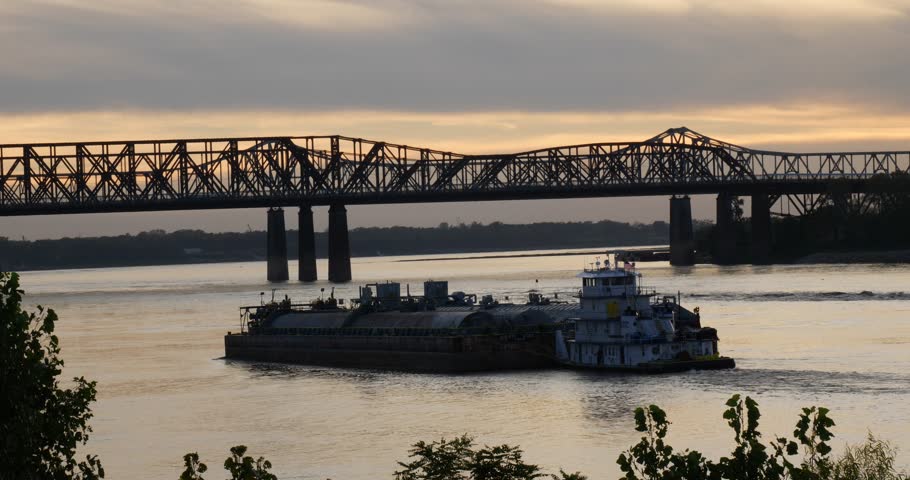 Cargo vessel cruising on the Mississippi River near Memphis Tennessee at dusk approaching a bridge over the river