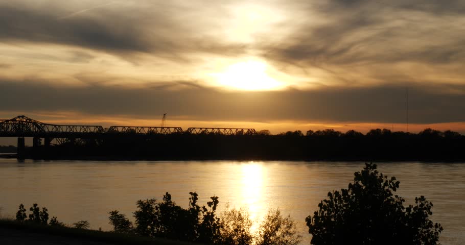 Colorful orange sunset over the Mississippi River casting a reflection over the water with vegetation in the foreground blowing in the breeze
