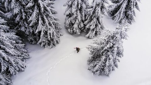 Snowboarder walking among trees with snowboard in hand. Aerial View. Walking in the snow forest.  Snowboard in the forest. Man Hiking With Snowboard Into Forest Back country Frozen  Forest. birds eye 