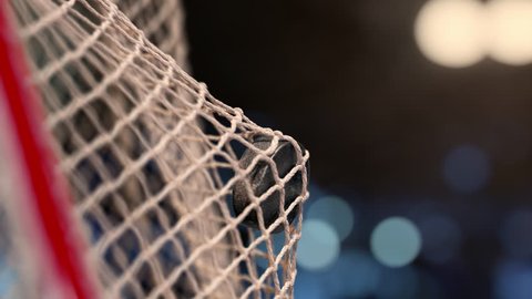 Hockey puck flies into the net on a stadium with yellow and blue lights. The movement at the beginning is accelerated then slowly. Beautiful close-up (4k, 3840x2160, ultra high definition)