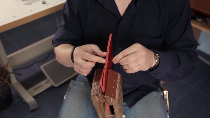 In the workshop, a man is sewing leather workpieces, making a wallet