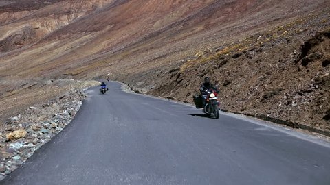 Spectacular scene with bikers riding motorcycles on Leh-Manali Highway flanked by rocky slopes of Himalaya mountains. Camera moves along road and passes by motorcyclists on bikes. Ladakh, India.