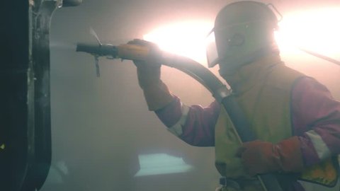 Industrial worker cleans metal surface by sandblaster gun