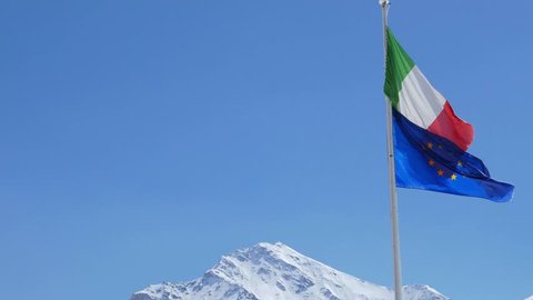 European Union and Italian flag blowing in the wind on the Alps, sunny clear blue sky