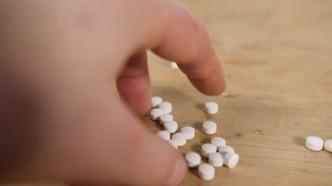Slow motion drug white pills falling onto wooden table from mans hand onto wooden table for headache prescription tablets