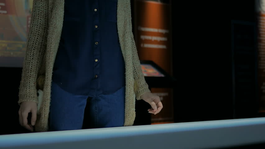 Woman using interactive touchscreen display in modern historical museum. Evening time, lowlight. Education and entertainment concept