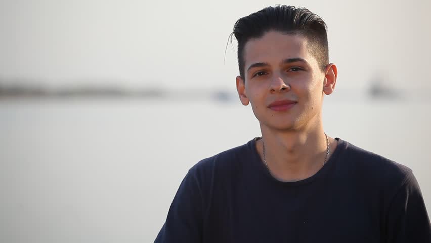 Young man in a black tshirt standing at a handrail on the Dnipro quay and smiling slightly on a sunny day in spring