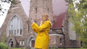a girl in a yellow raincoat talking on a video link near an old church