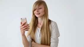 modern youth. beautiful long-haired girl of European appearance with blond hair expressively talking on a video communication smartphone near the white wall