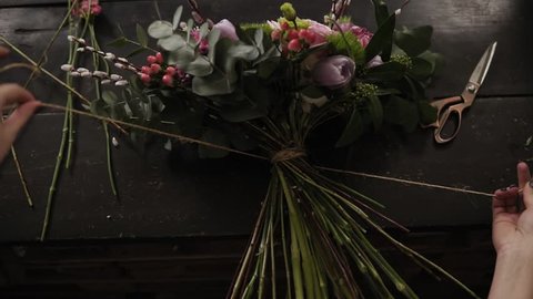 A beautiful bouquet of flowers decorated by a florist lies on a table. The girl tightly tightens it with rope on the stems. View from above