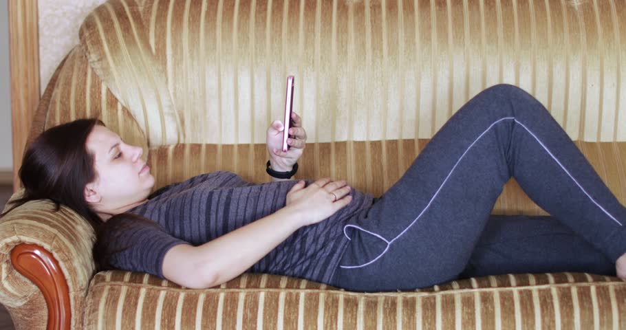On the couch is a pregnant girl with a smartphone and ironing her stomach