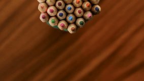 Many multicolored pencils move in a circle on a black wooden background. Concept office or school, knowledge day, the first of September. Video footage is spinning rotate