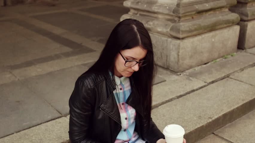 Dark girl with glasses, chatting with friends, drinking coffee and is on the street