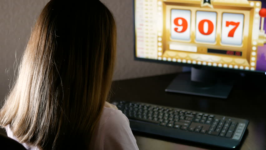 Young woman won in an online casino and coins pour out directly from the monitor. Brunette is very happy about her luck in gambling.