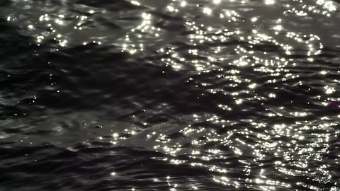 Looking over the calm water reflecting off the light. Slow Mo. High Contrast B&W Close Up Liquid Texture Seamless Loopable Abstract Motion Background. Shimmering and trembling ocean surface at sunset.