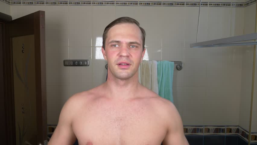 A handsome man smears a face with a cream in front of a mirror in the bathroom. 4k