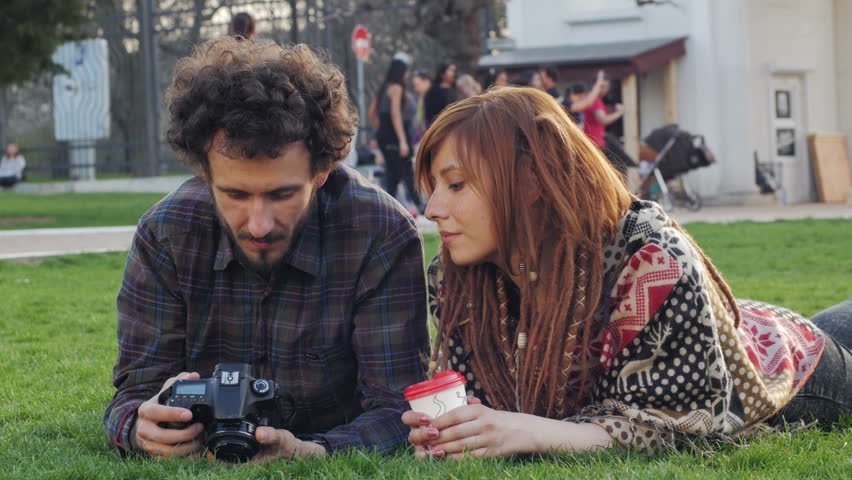 Young couple with photo camera relaxing and having fun on the green grass, dating in the summer park 