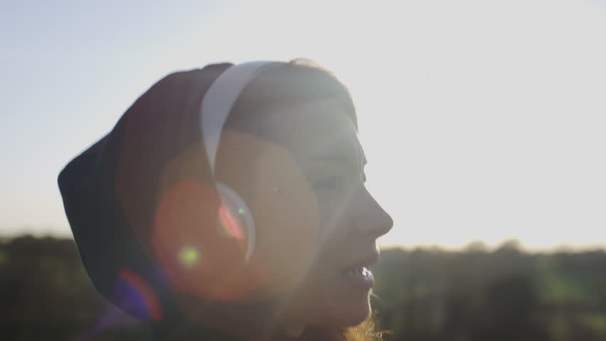 Young woman with headphones on walking and sings along happily outdoors in the countryside