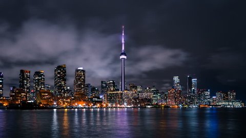 The downtown Toronto Canada city skyline with bright lights and moody storm clouds viewed from the porter island. Fast moving clouds in the sky in a quick paced urban environment. 