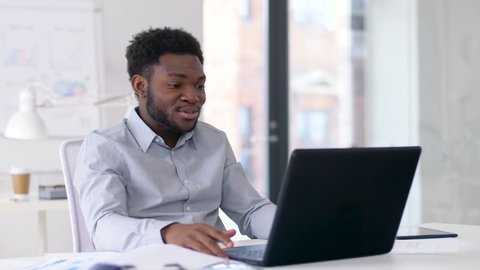 business, technology and communication concept - happy smiling african american businessman having video chat on laptop computer at office