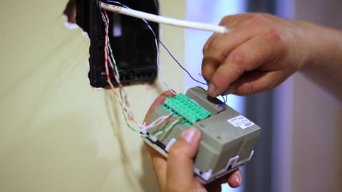 Worker hands connect wires to terminal block of electronic device.