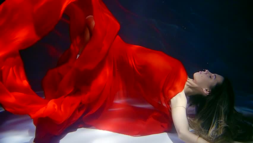 drowned woman is floating underwater in deepness in dark, her body is covered red chiffon fabric