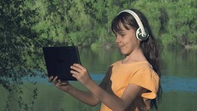Video call. A child with a tablet on the nature. Girl with a tablet on the river bank.
