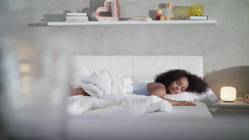 Young African American woman waking up at home. Portrait of happy black girl smiling, enjoying a large king size mattress all for herself. Slow motion Royalty-Free Stock Footage #1010458358