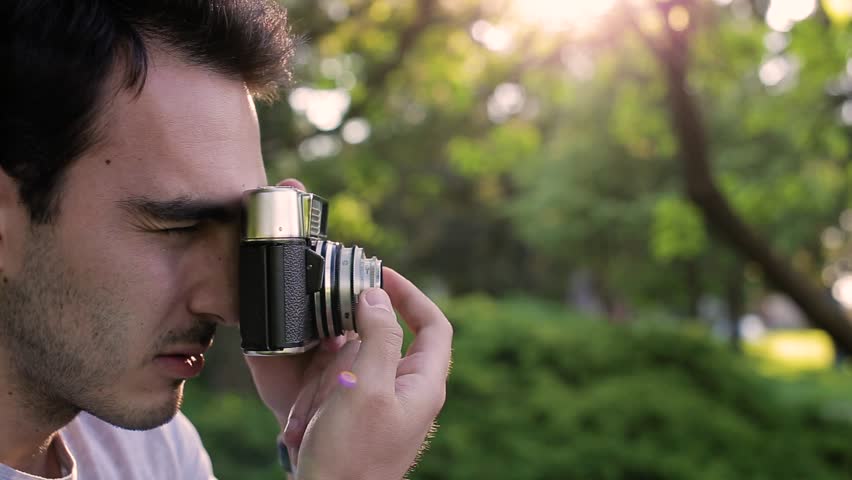Handsome man taking photos with analog camera at park