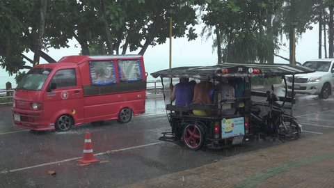 KRABI, THAILAND - MARCH 2017, SLOW MOTION: Local people sit and wait under a tarp for the monsoon to pass the silent coastal village during the tourist low season. Traffic during tropical rainstorm.