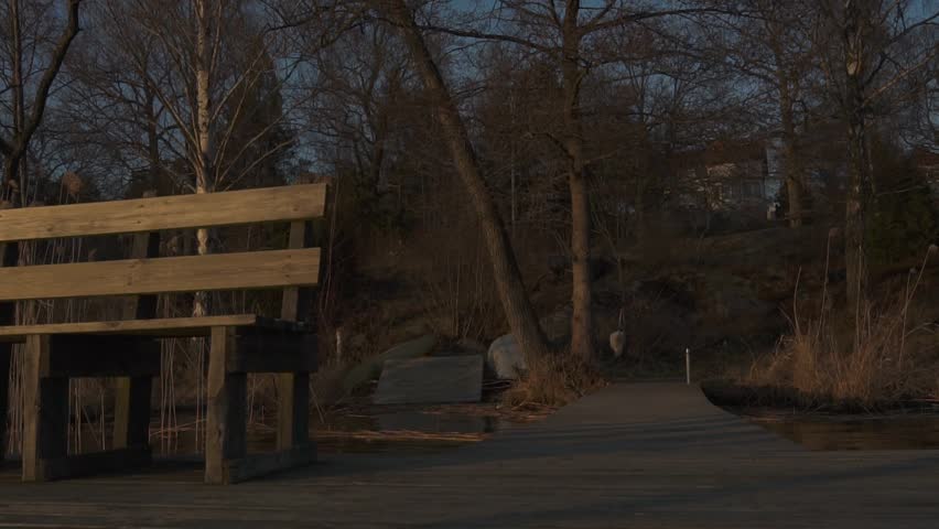 Golden light sunset revealing a bench and a wooden deck on the side of a lake. Slider shot.