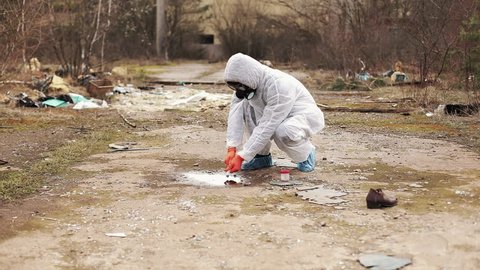 Man in bio-hazard suit and gas masks takes water and ground for the analysis