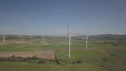 Flight near a wind power station in the daytime in the spring. Rotating blades of energy generators. Ecologically clean electricity. Modern technologies for the use of natural resources.