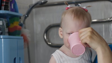 A little girl drinks water from a mug after brushing her teeth