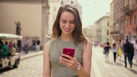 Attractive young woman in a bright sunlight uses phone walk in the city center strokes her hair looks around smile happy summer internet business outside technology eye spring mobile slow motion