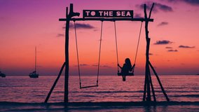 Silhouette beautiful girl riding on a swing on a tropical beach on a background of the sea and a scenic sunset