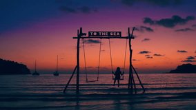 Summer vacation and lifestyle concept. Silhouette beautiful girl riding on a swing on a tropical beach on a background of the sea and a scenic sunset
