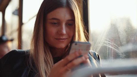 Portrait of attractive smiling girl in train using smartphone chatting with friends woman hand internet technology cellphone city mobile phone smartphone tram female transport young slow motion