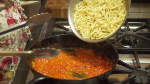 Close-up shot of a female cook mixing linguine pasta into a pan of hot sauce.