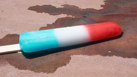 Time-lapse of a popsicle melting on a hot summer sidewalk at a picnic. The frozen ice cream treat melts in high speed showing the concept of heat waves and the rising temperatures of climate change.