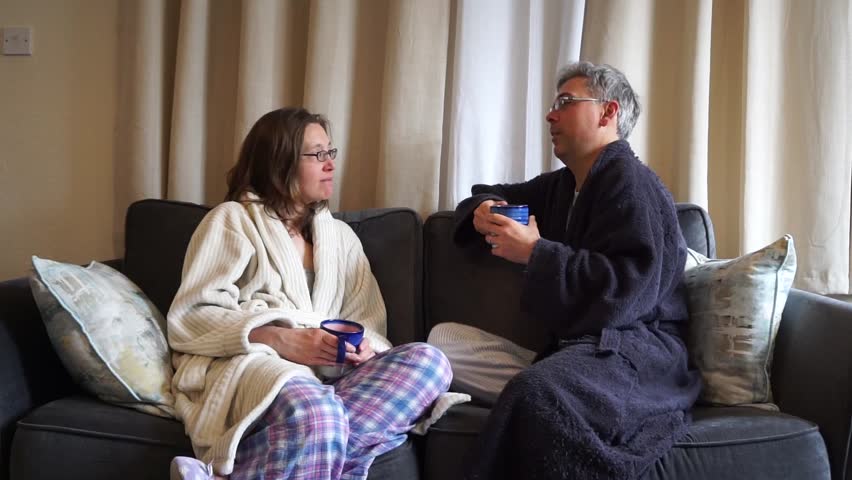 Couple (man and woman) wearing pajamas have an engaging morning conversation on a sofa while drinking coffee/tea. Royalty-Free Stock Footage #1010499272